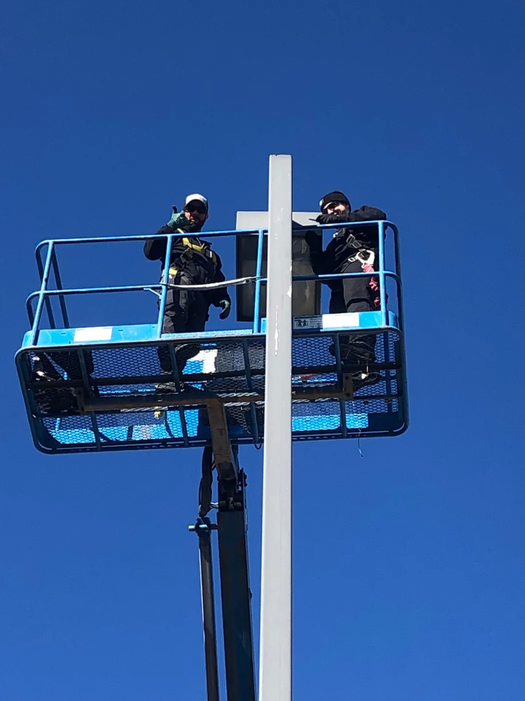 Electricians in a lift bucket servicing a parking lot pole light fixture